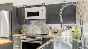Une cuisine moderne dotée d’appareils électroménagers en acier inoxydable, d’un dosseret de carrelage disposé en motif chevron et d’un évier encastré.