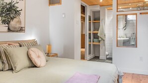 Une chambre à coucher comprenant un lit, une table de chevet, un miroir et une porte donnant sur une salle de bain.