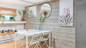 Une cuisine moderne avec une table et des chaises blanches, un miroir rond et des reproductions botaniques encadrées accrochées au mur.