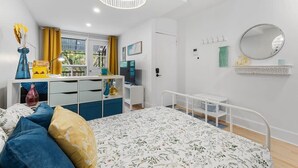 A modern bedroom with a bed, bedside tables, a desk, a chair, a hanging light fixture, a window with curtains, and a mirror on the wall.