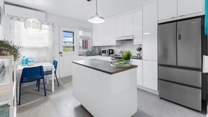 A modern kitchen with white cabinetry, a central island, stainless steel appliances, and a dining area with blue chairs.