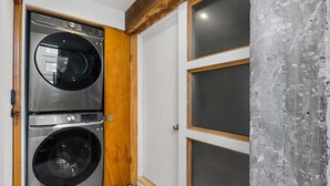 A laundry room with two stacked front-loading washers and dryers, a wooden door, and a concrete wall with a window.
