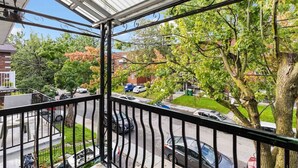 A balcony with a view of a residential street, a covered area with a metal railing, and a clear sky.
