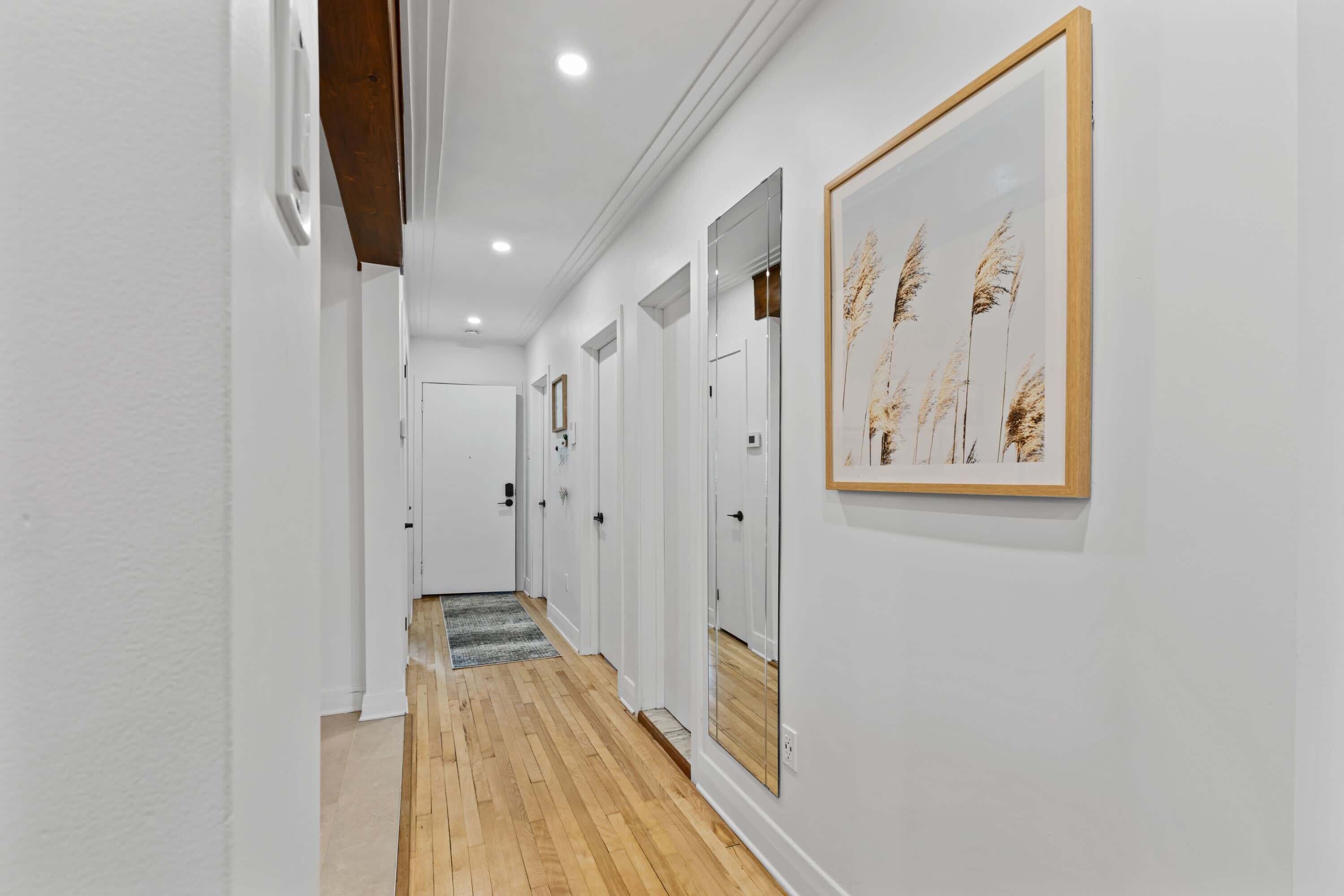 A hallway with white walls, wooden flooring, and framed artwork.
