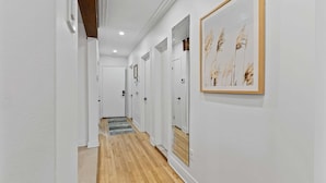 A hallway with white walls, wooden flooring, and framed artwork. - All-Inclusive Furnished Large 2BR Apartment in Rosemont (Montréal)