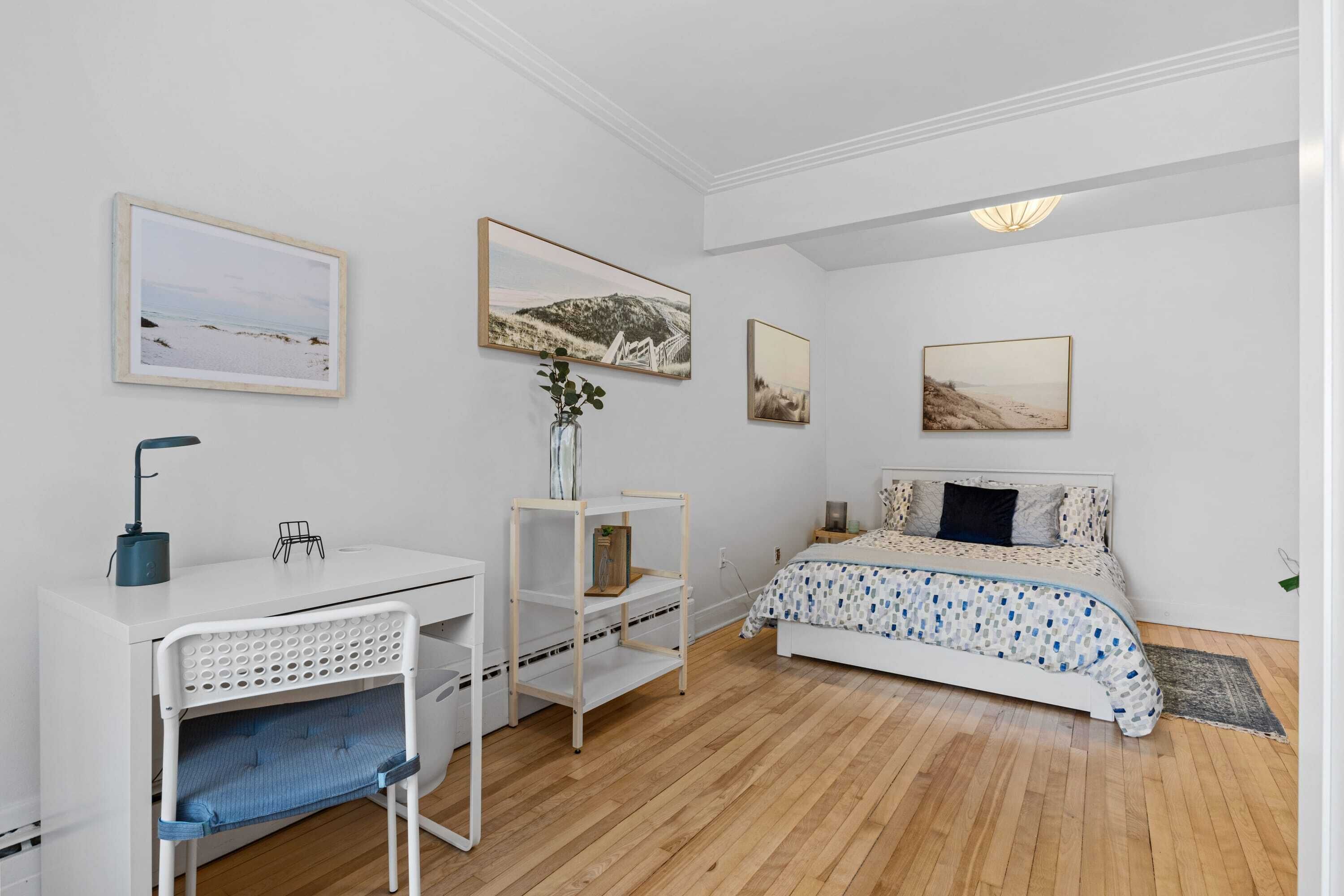 A bedroom with a bed, a desk, a chair, and wall art.