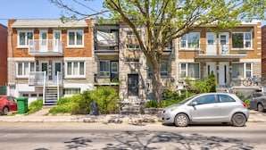 A row of townhouses with front porches, a tree in the center, and a silver car parked on the street. - All-Inclusive Furnished Large 2BR Apartment in Rosemont (Montréal)
