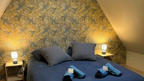 Un dormitorio con techo inclinado, cama con ropa oscura, dos lámparas de noche y un tragaluz.