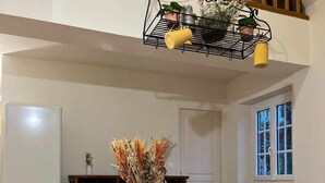 Un comedor con una mesa blanca, sillas de madera y un florero con flores secas.