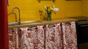 Una cocina con baldosas amarillas, un microondas blanco, un fregadero y una cortina con estampado floral.