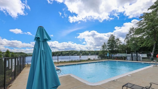 A swimming pool with a view of a lake, surrounded by trees and a fence.