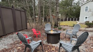 An outdoor seating area with a fire pit, four Adirondack chairs, and a gravel ground.