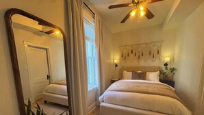 A bedroom with a large bed, a ceiling fan, a mirror, and a window with curtains.