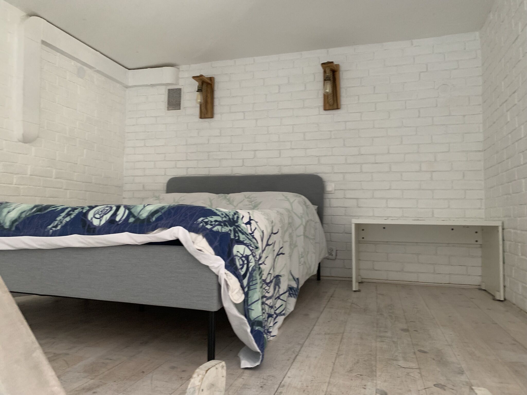 Une chambre à coucher avec un lit, une table de chevet et un mur en briques blanches.