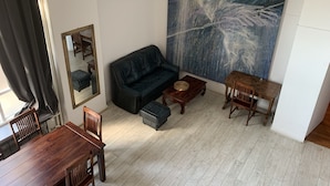 Un salon avec un canapé noir, une table basse en bois et une table à manger avec des chaises. Un grand tableau abstrait est accroché au mur, et il y a un miroir sur le mur.