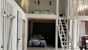 Une chambre à coucher aménagée dans un espace en hauteur, avec un lit superposé, une échelle et un fauteuil suspendu.