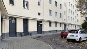 Un bâtiment doté de nombreuses portes et fenêtres, d’un trottoir pavé et de voitures garées.