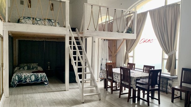 Une pièce comprenant un lit en mezzanine, un coin repas avec des chaises et une table en bois, ainsi qu’un escalier.