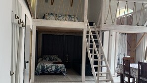 Une chambre à coucher aménagée dans un espace en hauteur, avec un lit superposé, une échelle en bois et un coin repas comprenant une table et des chaises.