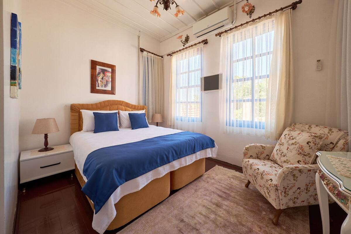 A bedroom with a bed, a nightstand, a chair, and a TV on the wall.