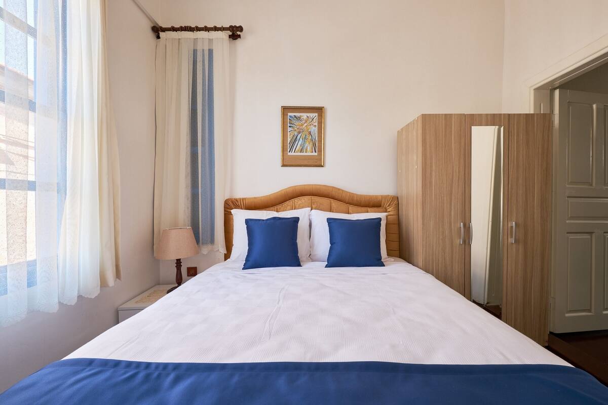 A neatly made bed with a white and blue bedspread, a wooden headboard, and a single blue pillow.