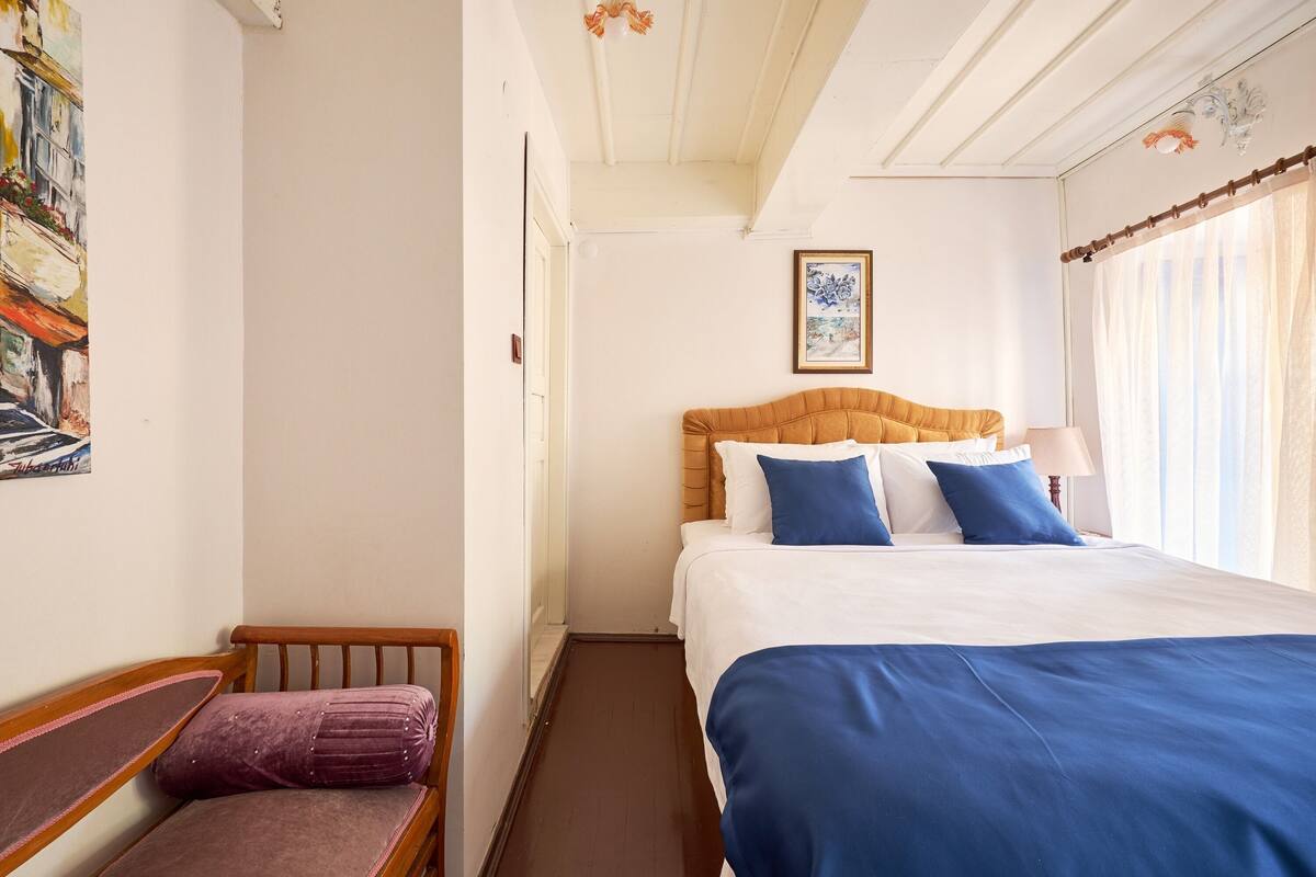 A hotel room with a bed, a bench, and a painting on the wall.