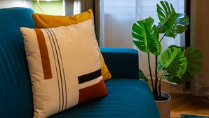 A modern living room with a teal sofa, a potted monstera plant, and a view of the city through sheer curtains. - Budapest Holidays Courtyard (Budapest)