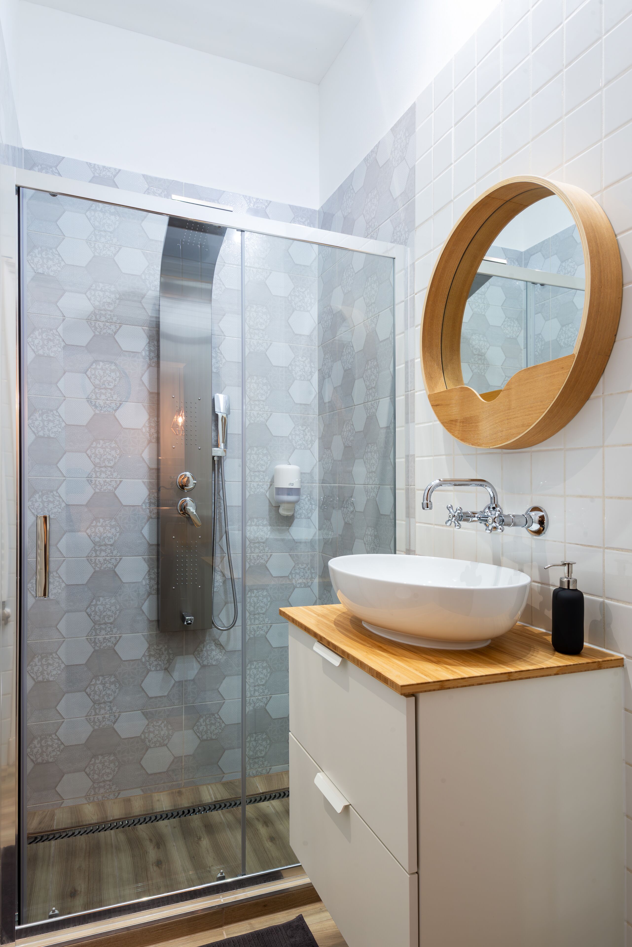 Ein modernes Badezimmer mit einer ein Glasfach werkseitig installierten Dusche, einem Holzwaschtisch mit weißem Waschbecken und einem runden Spiegel.