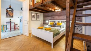 A bedroom with a wooden ceiling, a bed with yellow and white bedding, a wooden ladder, and a small table with stools. - Budapest Holidays Courtyard (Budapest)