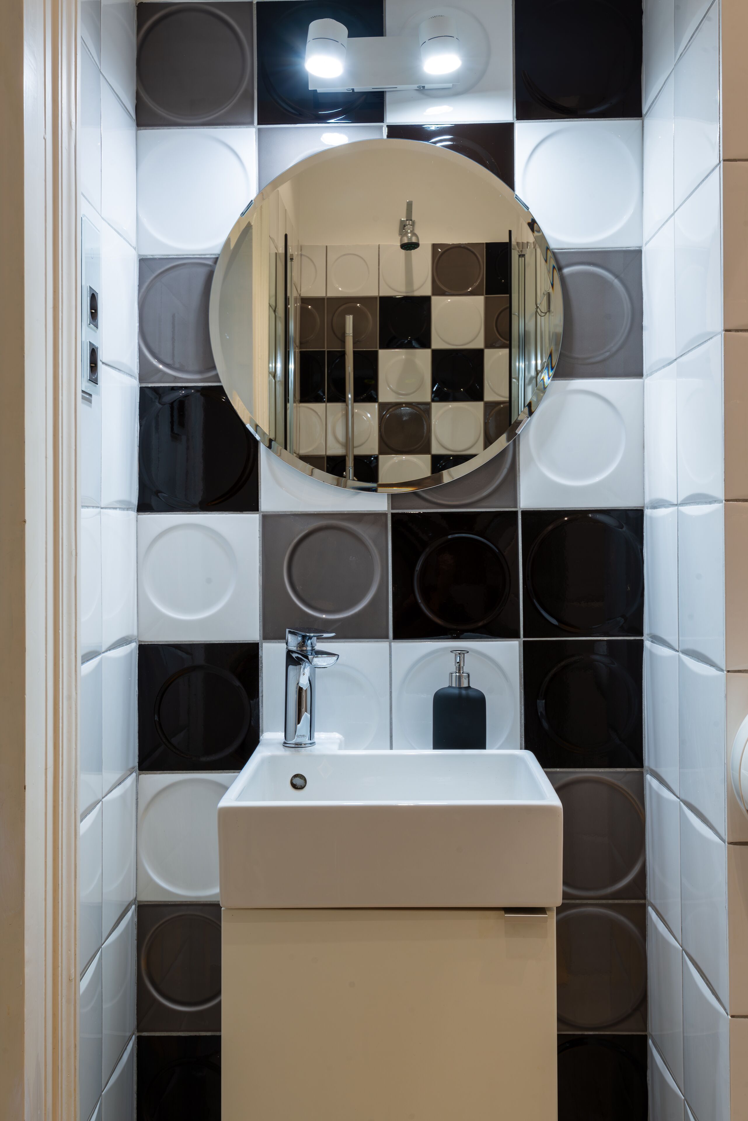 A bathroom with a checkered tile wall, a round mirror, and a white sink with a soap dispenser.