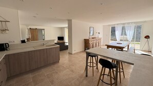 A modern kitchen with a central island, a dining area with stools, and a large window offering a view of the outdoors. - Gîte rdc Villa - Village Provençal - Proche Uzès (Le Pin)