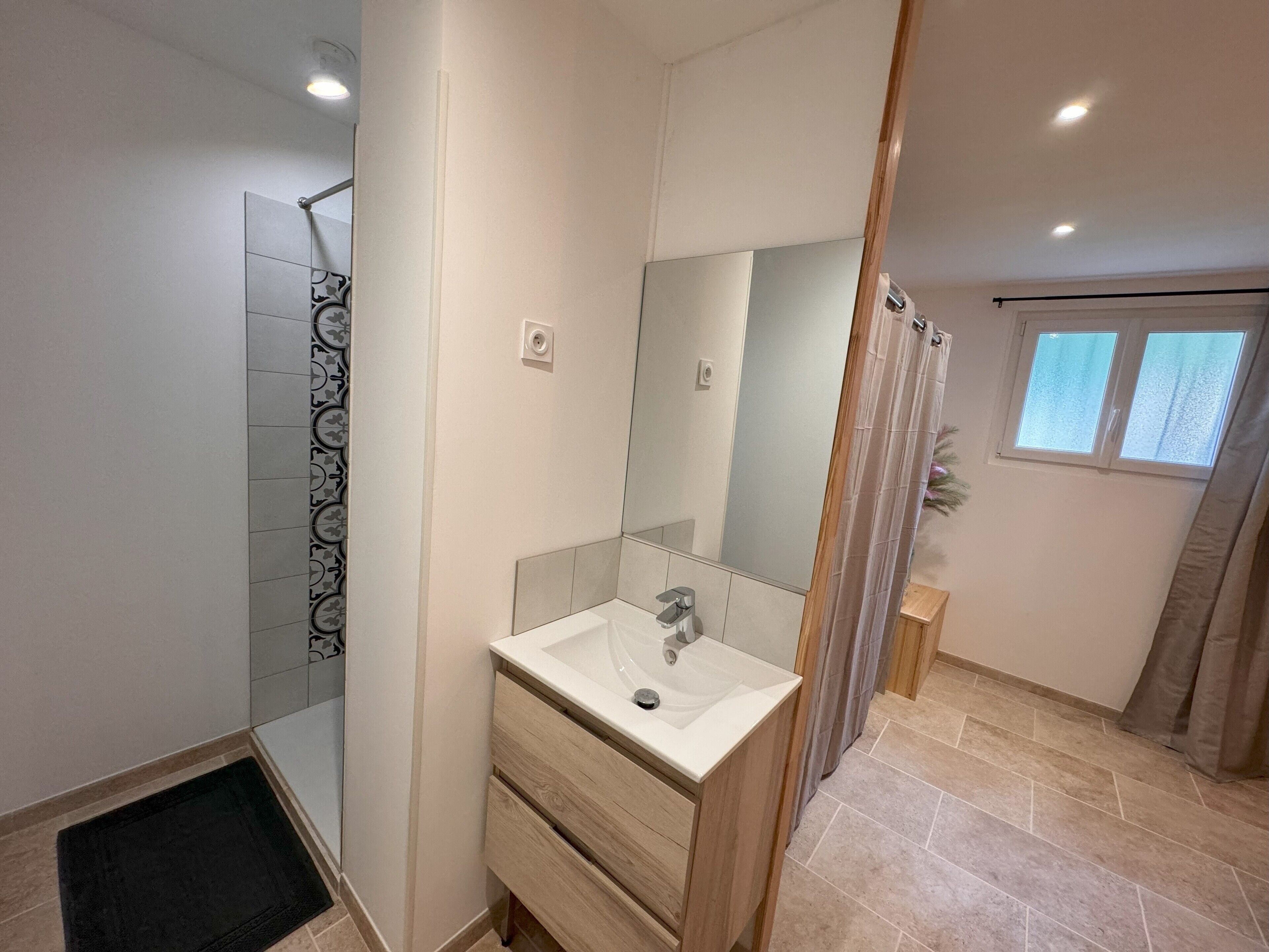 Une salle de bain moderne avec une douche, un lavabo avec un miroir et une fenêtre.
