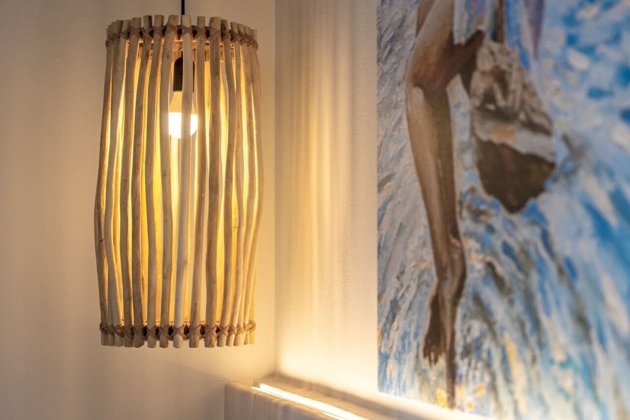 A wooden slatted pendant light fixture and a painting of a person in a blue and white abstract style.