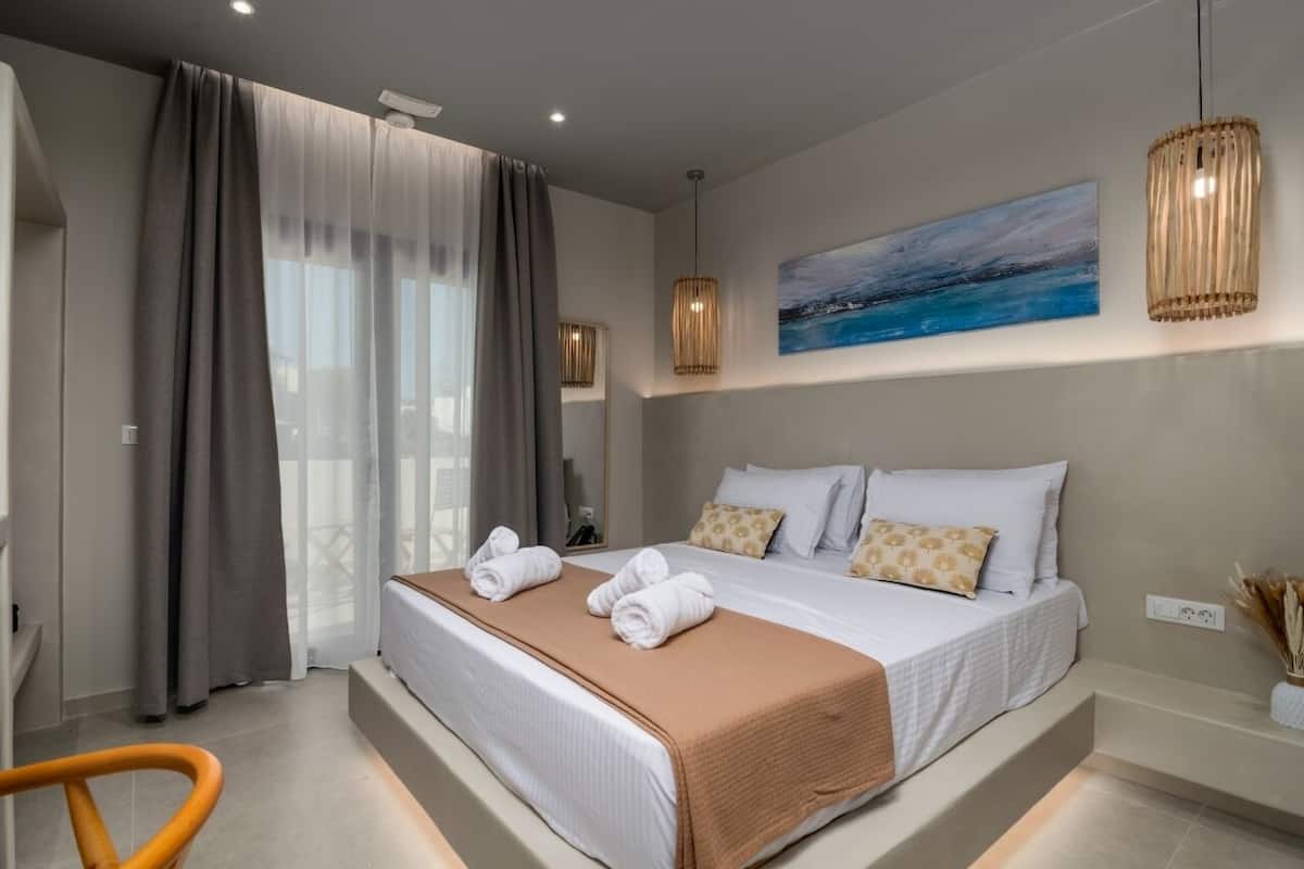 A modern hotel bedroom with a large bed, a view of the sea through the window, and a painting on the wall.