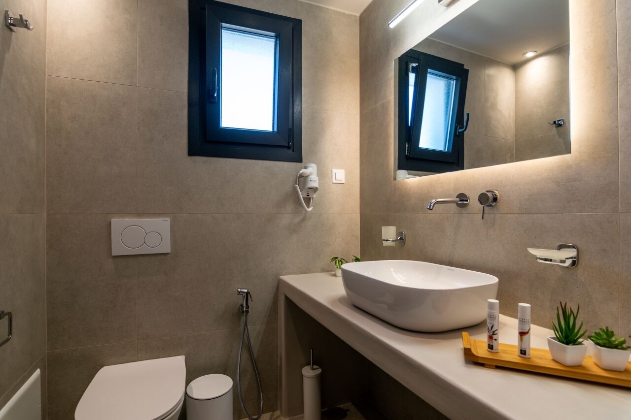 A modern bathroom with a large white sink, a toilet, a shower, and a mirror with a window above it.