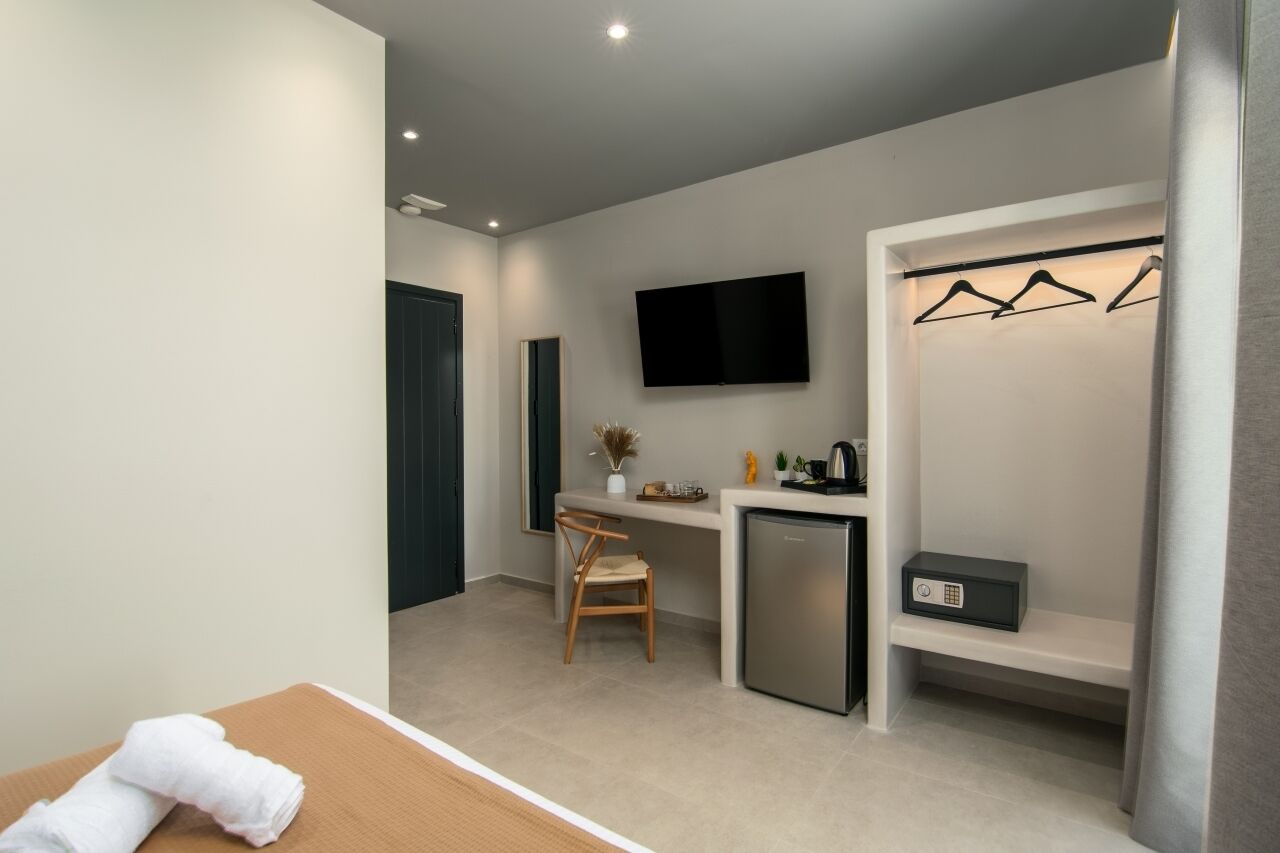 Ein kleines Hotelzimmer mit einem Bett, einem kleinen Schreibtisch, einem Fernseher und einem Kleiderschrank mit Kleidung.