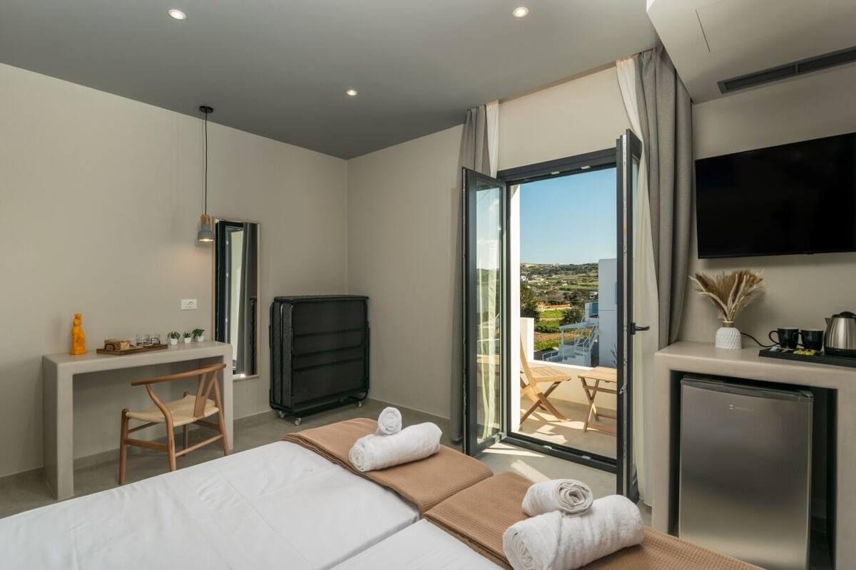 A modern hotel room with a bed, desk, and a balcony with a view.