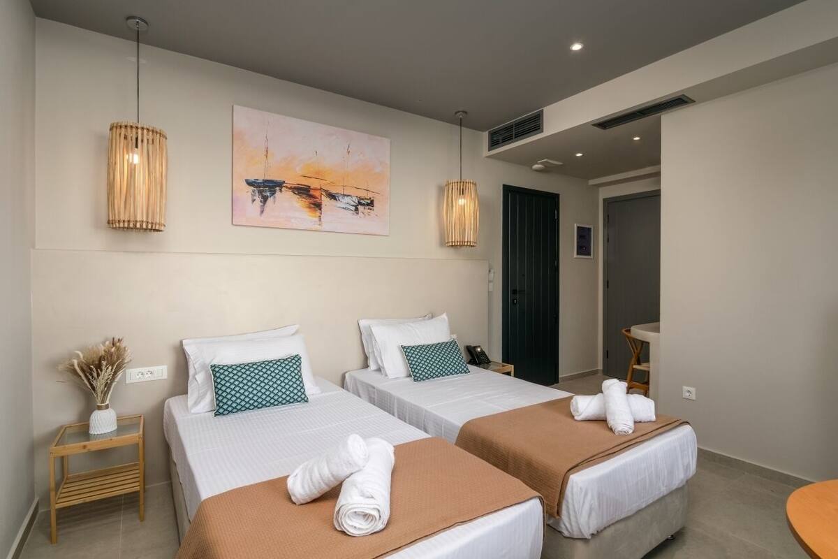 A hotel room with two beds, a painting on the wall, and a small table with a vase of dried plants.