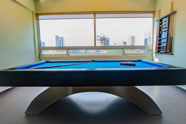 Une table de billard dans une pièce dotée d’une grande fenêtre donnant sur un paysage urbain.