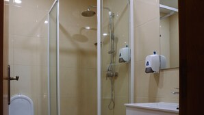 Un box de ducha con paredes de vidrio, un cabezal de ducha manual y un secador de manos incorporado en la pared.