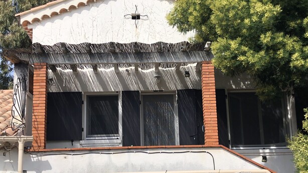 A building with a white facade, a tiled roof, and a balcony with a patterned awning. - Small independent 2-room flat (Cavalaire)