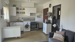 A compact living space with a kitchenette, a washing machine, a small oven, and a sofa with a throw pillow. - Small independent 2-room flat (Cavalaire)