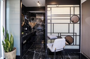 Un interior moderno con suelo de mármol negro, una planta en maceta, una silla y una pared decorativa con patrones geométricos.