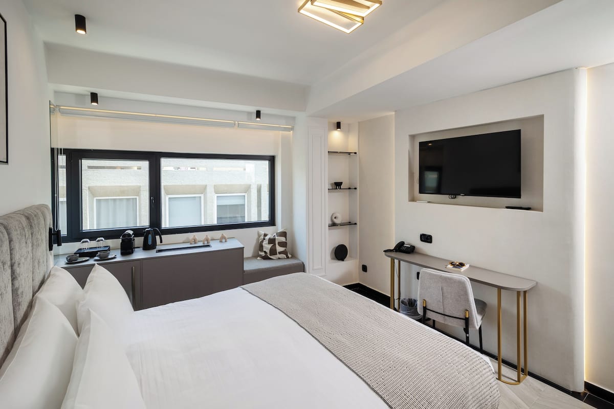 Une chambre d’hôtel moderne dotée d’un grand lit, d’un bureau, d’une télévision et d’une fenêtre donnant sur la ville.
