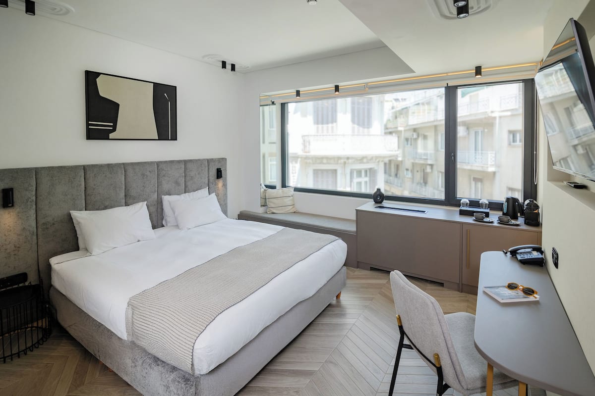 Une chambre moderne avec un grand lit, un bureau et une fenêtre donnant sur la ville.