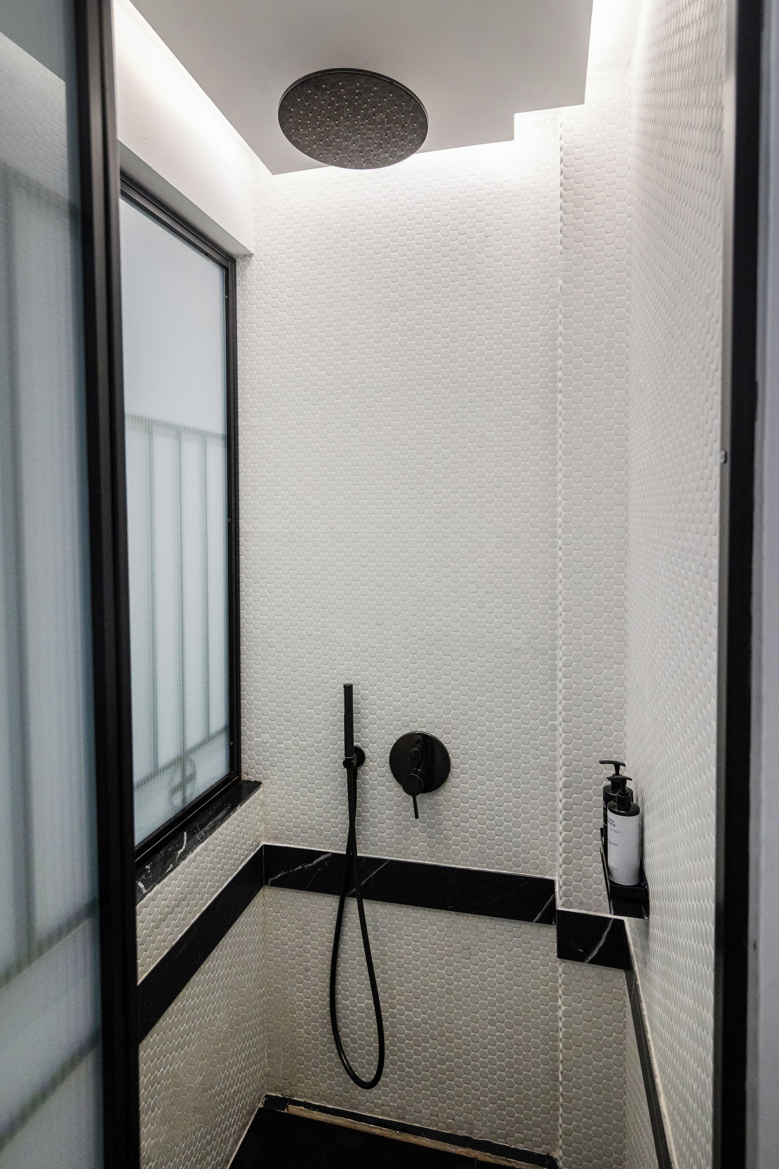 Casa de banho pequena e moderna com chuveiro, janela e dispensador de sabonete.
