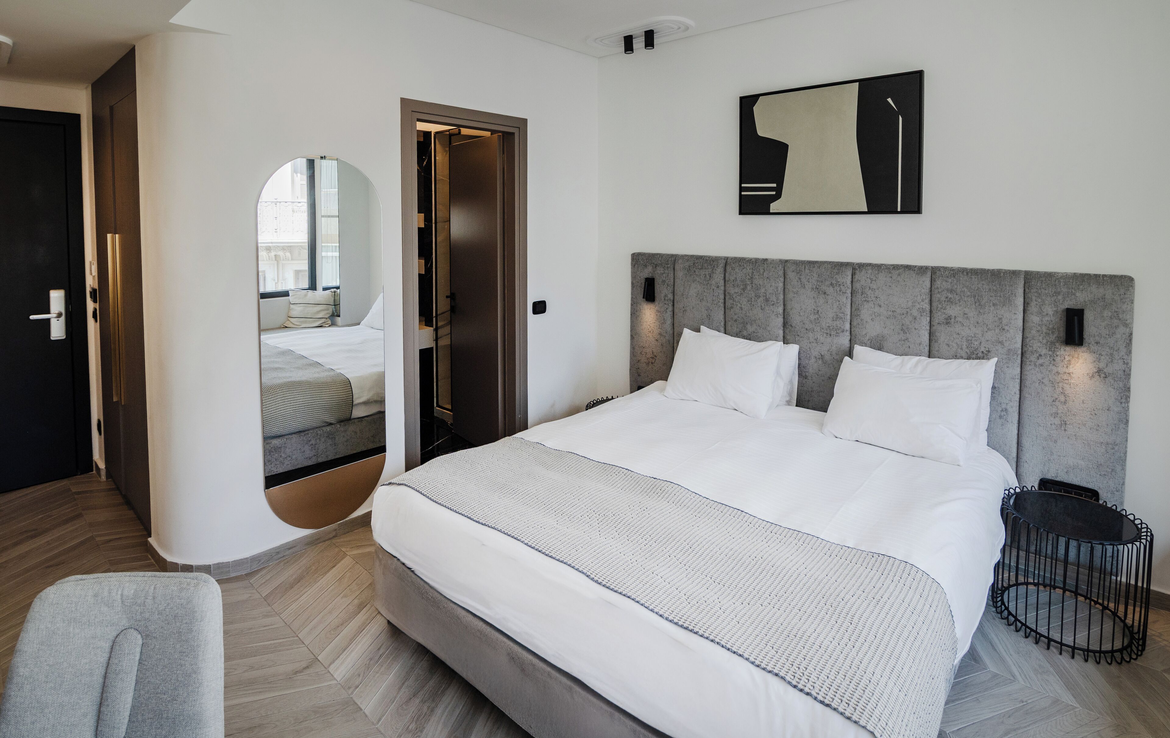 Quarto de hotel moderno com uma cama grande, um espelho redondo e vista da cidade pela janela.