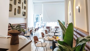 A modern dining area with multiple tables and chairs, a decorative wall with recessed lighting, and a large plant in the foreground. - Esse Athens (Athens)
