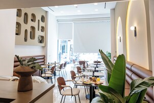 Un área de comedor moderna con varias mesas y sillas, una pared decorativa con iluminación empotrada y una planta grande al frente.