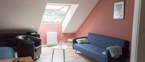 A cozy living room with a sloped ceiling, a blue sofa, a coffee table, and a view through a skylight.